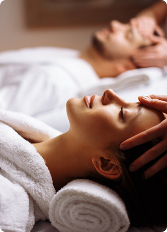 Woman lying on a massage table with a therapist performing a head massage in a relaxing spa environment.